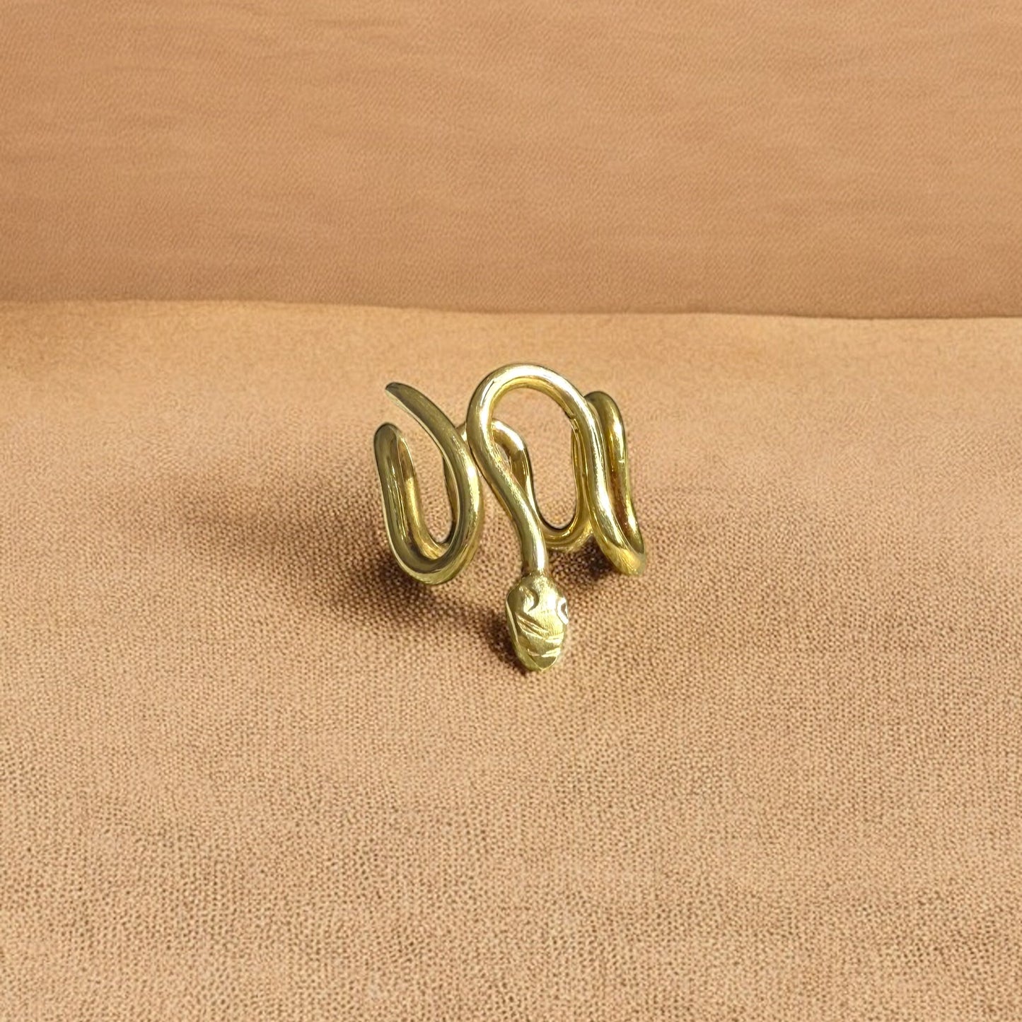 The ring called Gbeto is placed on a flat surface. The ring is made of African brass, with a snake wrapped shape.