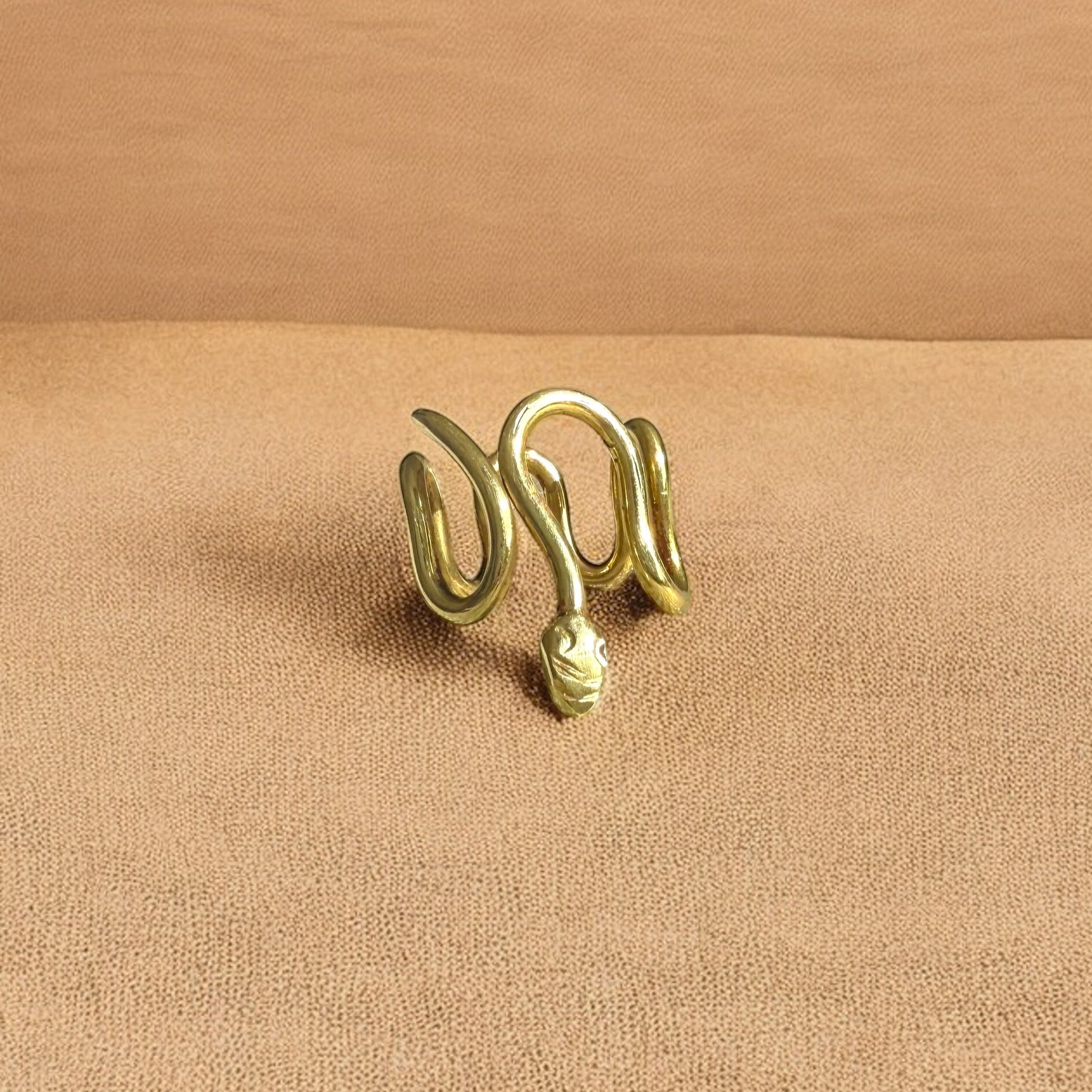 The ring called Gbeto is placed on a flat surface. The ring is made of African brass, with a snake wrapped shape. 